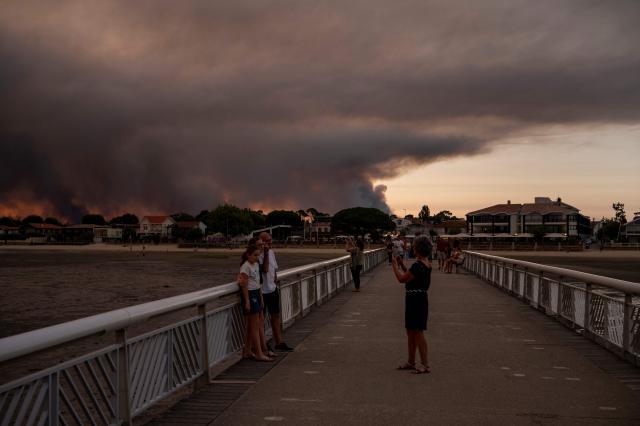 People pose on the beach in Andernos-Les Bains during a fire in Lege Cap-Ferret forest, southwestern France, on July 23, 2026, as part of the nearby area has been evacuated. A highly virulent wildfire has swept through more than 3700 hectares since July 22, 2026 near the Arcachon Basin (Gironde), where nearly 20,000 residents and tourists have been evacuated in total from this area of the Landes de Gascogne forest, already devastated by flames in 2022. (Photo by Olivier MORIN / AFP)