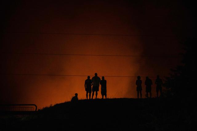 People watch as a forested area burn close to a residential area during a wildfire near Lege-Cap-Ferret, southwestern France, on July 23, 2026. A highly virulent wildfire has swept through more than 3700 hectares since July 22, 2026 near the Arcachon Basin (Gironde), where nearly 20,000 residents and tourists have been evacuated in total from this area of the Landes de Gascogne forest, already devastated by flames in 2022. (Photo by JULIEN DE ROSA / AFP)