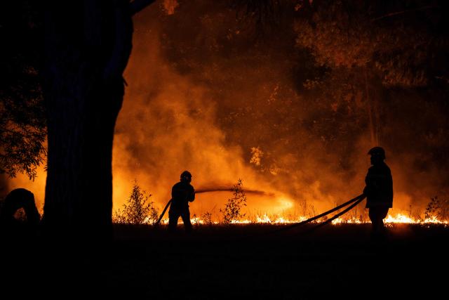 Firefighters spray water on a burning forest close to a residential area during a wildfire near Lege-Cap-Ferret, southwestern France, on July 23, 2026. A highly virulent wildfire has swept through more than 3700 hectares since July 22, 2026 near the Arcachon Basin (Gironde), where nearly 20,000 residents and tourists have been evacuated in total from this area of the Landes de Gascogne forest, already devastated by flames in 2022. (Photo by JULIEN DE ROSA / AFP)