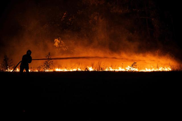 A firefighter sprays water on a burning forested area close to a residential area during a wildfire near Lege-Cap-Ferret, southwestern France, on July 23, 2026. A highly virulent wildfire has swept through more than 3700 hectares since July 22, 2026 near the Arcachon Basin (Gironde), where nearly 20,000 residents and tourists have been evacuated in total from this area of the Landes de Gascogne forest, already devastated by flames in 2022. (Photo by JULIEN DE ROSA / AFP)