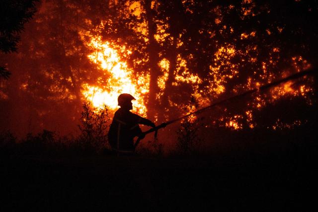A firefighter sprays water on a burning forest close to a residential area during a wildfire near Lege-Cap-Ferret, southwestern France, on July 23, 2026. A highly virulent wildfire has swept through more than 3700 hectares since July 22, 2026 near the Arcachon Basin (Gironde), where nearly 20,000 residents and tourists have been evacuated in total from this area of the Landes de Gascogne forest, already devastated by flames in 2022. (Photo by JULIEN DE ROSA / AFP)
