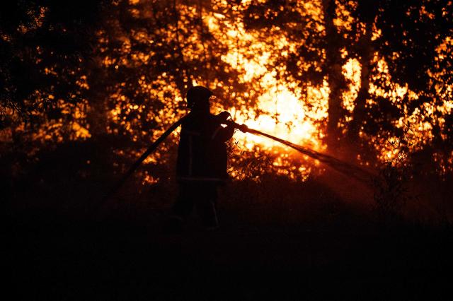 A firefighter sprays water on a burning forest close to a residential area during a wildfire near Lege-Cap-Ferret, southwestern France, on July 23, 2026. A highly virulent wildfire has swept through more than 3700 hectares since July 22, 2026 near the Arcachon Basin (Gironde), where nearly 20,000 residents and tourists have been evacuated in total from this area of the Landes de Gascogne forest, already devastated by flames in 2022. (Photo by JULIEN DE ROSA / AFP)