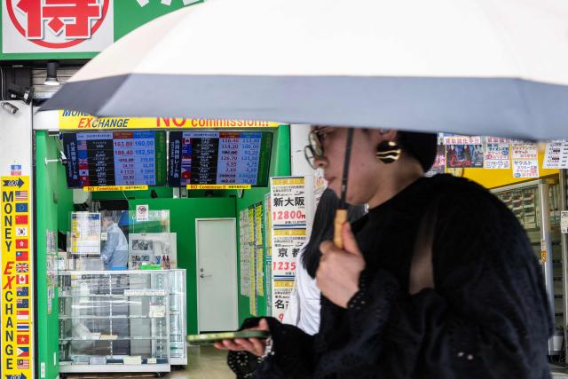 A woman walks past a display showing currency rates at a money exchange in Shinjuku district in Tokyo on July 24, 2026. Core inflation accelerated in Japan in June, official data showed as the Middle East war and a weak yen pushed up prices for consumers in the world's fourth-biggest economy. A falling yen, which overnight hit a fresh four-decade low against the US dollar, also increases the cost of imports like oil and food for resource-poor Japan. (Photo by Andrew CABALLERO-REYNOLDS / AFP)