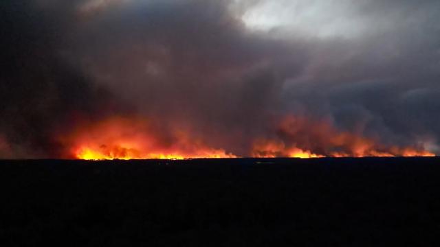 This frame grab from an AFP TV video shows an aerial view taken from Ares on July 24, 2026 showing a vast wall of flames lighting up the night as a wildfire burns through Lege-Cap-Ferret near the Cap Ferret peninsula. The fire, which is thought to have started accidentally and has been ravaging the forest north of the Arcachon Basin (Gironde) since July 22, threatening Lege-Cap-Ferret, has now spread across 8,700 hectares, according to the prefecture, which on July 24 ordered the evacuation by road and sea of the entire Cap-Ferret peninsula, a popular tourist destination. France has been battered by three heatwaves since May as part of increasingly common extreme weather episodes linked to climate change, causing excess deaths, drying up rivers and fuelling wildfires. Scientists have long warned that climate change caused by human use of fossil fuels will make periods of drought more intense and longer-lasting, creating the ideal conditions for wildfires. (Photo by AFP)