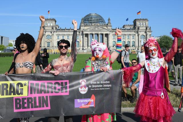 Participants react in front of the Reichstag building in Berlin, which houses Germany's Bundestag lower house of parliament, during the start of the Drag Queen March on July 24, 2026. Ahead of the Christopher Street Day (CSD) parade, Berlin hosts its first-ever Drag March bringing a tradition known from New York to Berlin. (Photo by RALF HIRSCHBERGER / AFP)