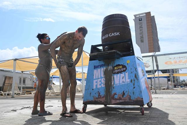 Tourists cover their bodies with mud during the 29th Boryeong Mud Festival at Daecheon Beach in Boryeong on July 25, 2026, which runs from July 24 to August 9 and aims to promote the use of mud for cosmetic skincare and tourism in the region. (Photo by Jung Yeon-je / AFP)