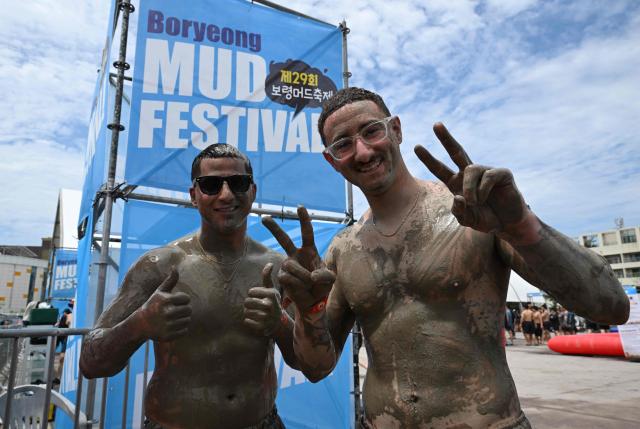 Tourists covered with mud pose for a photo during the 29th Boryeong Mud Festival at Daecheon Beach in Boryeong on July 25, 2026, which runs from July 24 to August 9 and aims to promote the use of mud for cosmetic skincare and tourism in the region. (Photo by Jung Yeon-je / AFP)