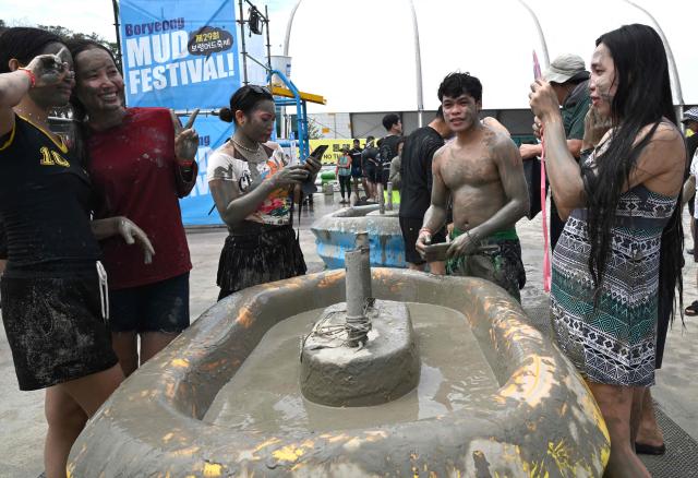 Tourists covered with mud pose for a photo during the 29th Boryeong Mud Festival at Daecheon Beach in Boryeong on July 25, 2026, which runs from July 24 to August 9 and aims to promote the use of mud for cosmetic skincare and tourism in the region. (Photo by Jung Yeon-je / AFP)