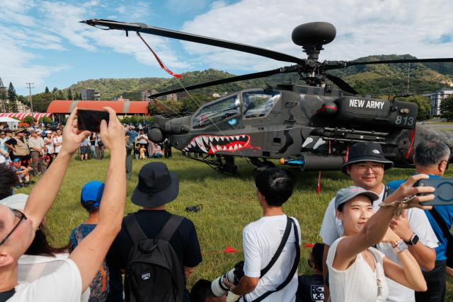 Visitors pose for photos in front of an AH-64E Apache attack helicopter displayed during an open day at the National Defence University’s Fuxinggang campus in Taipei on July 25, 2026. (Photo by CHENG Yu-chen / AFP)