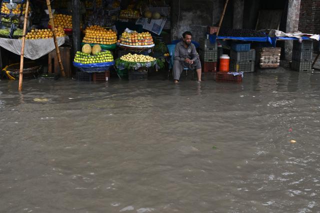 A fruit vendor waits for customers along a flooded street after heavy rainfall in Lahore on July 25, 2026. (Photo by Arif ALI / AFP)