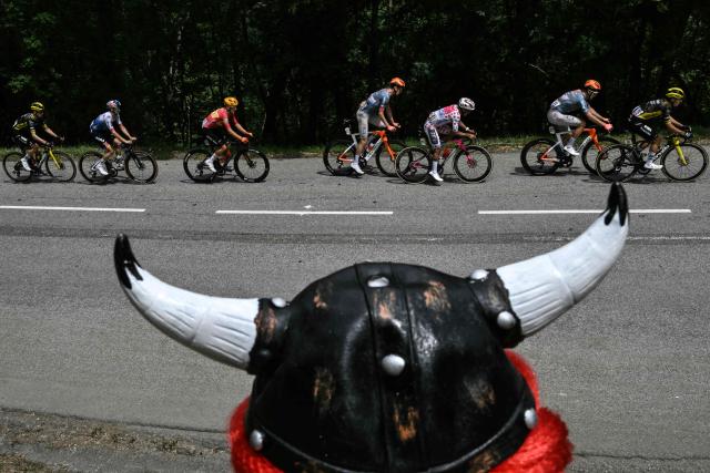 The lead breakaway cycles past a spectator wearing a helmet with horns in the Col du Galibier ascent during the 20th stage of the 113th edition of the Tour de France cycling race, 170,9 km between Le Bourg-d'Oisans and Alpe d'Huez in the French Alps, on July 25, 2026. (Photo by Jeff PACHOUD / AFP)