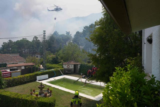 A firefighter helicopter dumps water as firefighters collect water from a swimmming pool while battling a fire surrounding La Atalaya residential area in El Tiemblo, 80 kms west of Madrid, on July 25, 2026 amid wildfires that have burned up to 25,000 hectares. Spanish firefighters hoped to get control of wildfires raging near Madrid on Saturday but an official warned that erratic winds threatened to fan the blazes further. The worst wildfires in the Madrid region's history rage west of the Spanish capital, forcing authorities to evacuate or order around 60,000 people to remain indoors. (Photo by Cesar MANSO / AFP)