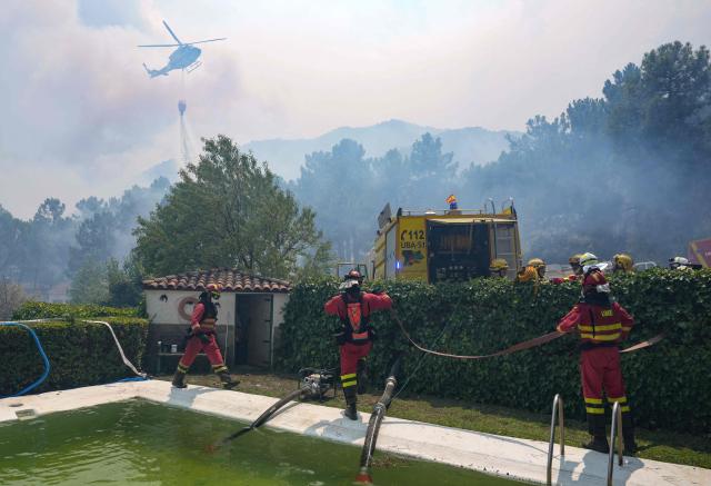 A firefighter helicopter dumps water as firefighters collect water from a swimmming pool while battling a fire surrounding La Atalaya residential area in El Tiemblo, 80 kms west of Madrid, on July 25, 2026 amid wildfires that have burned up to 25,000 hectares. Spanish firefighters hoped to get control of wildfires raging near Madrid on Saturday but an official warned that erratic winds threatened to fan the blazes further. The worst wildfires in the Madrid region's history rage west of the Spanish capital, forcing authorities to evacuate or order around 60,000 people to remain indoors. (Photo by Cesar MANSO / AFP)