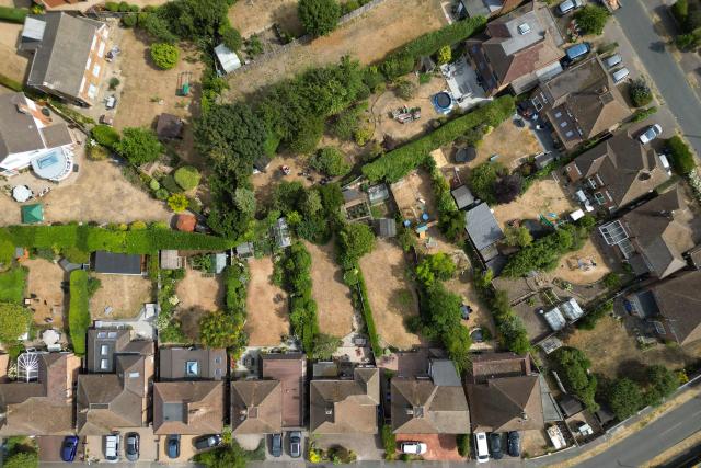 An aerial view shows parched gardens with dried and yellowed grass on residential streets in Woking , west of London on July 25, 2026, during the extended heatwave. Several areas of southern England were at "exceptional" risk of major wildfires, according to government advisory body Natural England, as Britain has faced unprecedented heatwaves for much of the last two months. (Photo by Justin TALLIS / AFP)