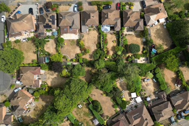 An aerial view shows parched gardens with dried and yellowed grass on residential streets in Woking , west of London on July 25, 2026, during the extended heatwave. Several areas of southern England were at "exceptional" risk of major wildfires, according to government advisory body Natural England, as Britain has faced unprecedented heatwaves for much of the last two months. (Photo by Justin TALLIS / AFP)