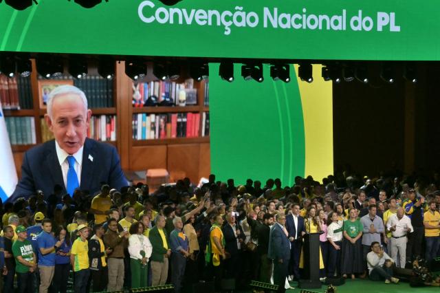 Israel's Prime Minister Benjamin Netanyahu speaks via videoconference to support the candidacy of right-wing presidential hopeful Flavio Bolsonaro during the Liberal Party (PL) convention, in Sao Paulo, Brazil on July 25, 2026. Battered by a string of political crises, Flavio Bolsonaro launched his candidacy for Brazil's October presidential election, seeking to follow in the footsteps of his father, Jair Bolsonaro, who is serving house arrest for plotting a coup after losing the election in 2022. (Photo by Nelson ALMEIDA / AFP)
