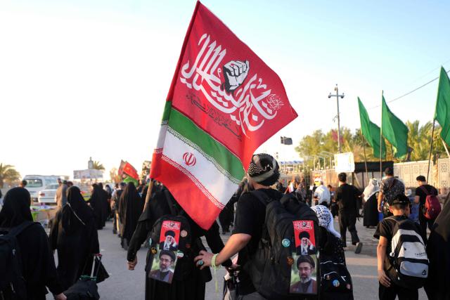 Iranian pilgrims walk along the highway from the holy Shia Muslim city of Najaf to Karbala, some 80 kilometers away, as they march to commemorate the Arbaeen or 40 days of mourning after the martyrdom in the Battle of Karbala in 680 CE of Imam Hussein, the grandson of the Prophet Muhammad, on July 25, 2026. Over the past two days, thousands of Iranian pilgrims have arrived in the city of Najaf before heading on foot to the holy city of Karbala to commemorate the Arbaeen of Imam Hussein, carrying Iranian flags and portraits of former Iranian Supreme Leader Ayatollah Ruhollah Khomeini, Supreme Leader Ali Khamenei, and Mojtaba Khamenei. The arrival of Iranian pilgrims in Iraq comes despite the ongoing war between the US and Iran, as pilgrims continue their journey toward Karbala to participate in the Arbaeen pilgrimage. (Photo by Qassem al-KAABI / AFP)