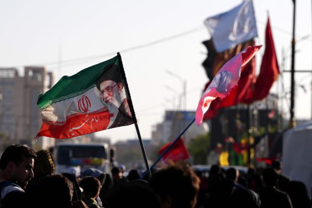 Iranian pilgrims walk along the highway from the holy Shia Muslim city of Najaf to Karbala, some 80 kilometers away, as they march to commemorate the Arbaeen or 40 days of mourning after the martyrdom in the Battle of Karbala in 680 CE of Imam Hussein, the grandson of the Prophet Muhammad, on July 25, 2026. Over the past two days, thousands of Iranian pilgrims have arrived in the city of Najaf before heading on foot to the holy city of Karbala to commemorate the Arbaeen of Imam Hussein, carrying Iranian flags and portraits of former Iranian Supreme Leader Ayatollah Ruhollah Khomeini, Supreme Leader Ali Khamenei (image on the flag), and Mojtaba Khamenei. The arrival of Iranian pilgrims in Iraq comes despite the ongoing war between the US and Iran, as pilgrims continue their journey toward Karbala to participate in the Arbaeen pilgrimage. (Photo by Qassem al-KAABI / AFP)