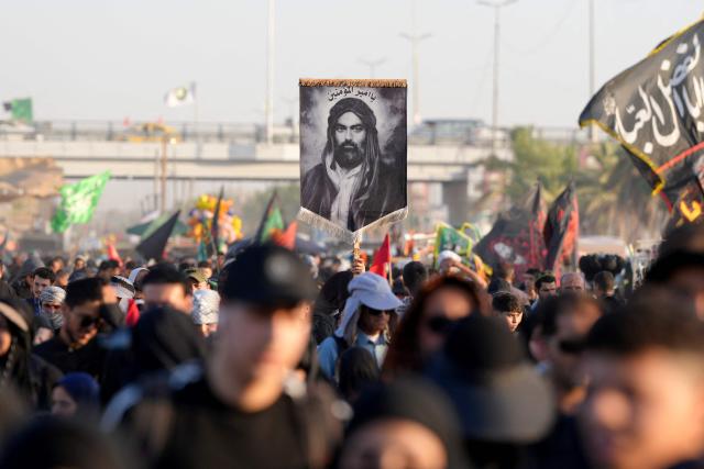 TOPSHOT - Iranian pilgrims hold up an image of the cousin and son-in-law of Islam's Prophet Muhammad, Imam Ali ibn Abi Talib with the inscription reserved to him, 'Amir al-Mu'minin (Commander of the Faithful), as they walk along the highway from the holy Shia Muslim city of Najaf to Karbala, some 80 kilometers away, to commemorate the Arbaeen or 40 days of mourning after the martyrdom in the Battle of Karbala in 680 CE of Imam Hussein, the grandson of the Prophet, on July 25, 2026. Over the past two days, thousands of Iranian pilgrims have arrived in the city of Najaf before heading on foot to the holy city of Karbala to commemorate the Arbaeen of Imam Hussein, carrying Iranian flags and portraits of former Iranian supreme leaders. The arrival of Iranian pilgrims in Iraq comes despite the ongoing war between the US and Iran, as pilgrims continue their journey toward Karbala to participate in the Arbaeen pilgrimage. (Photo by Qassem al-KAABI / AFP)