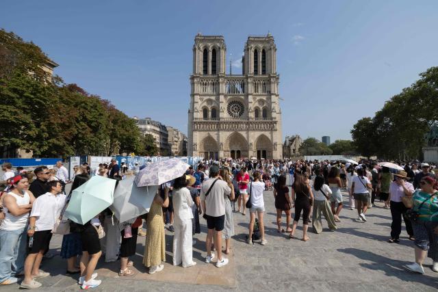 Tourists use umbrellas to shield themselves from the sun as they queue to visit Notre-Dame Cathedral during a hot summer day in Paris on July 25, 2026. (Photo by Xavier GALIANA / AFP)