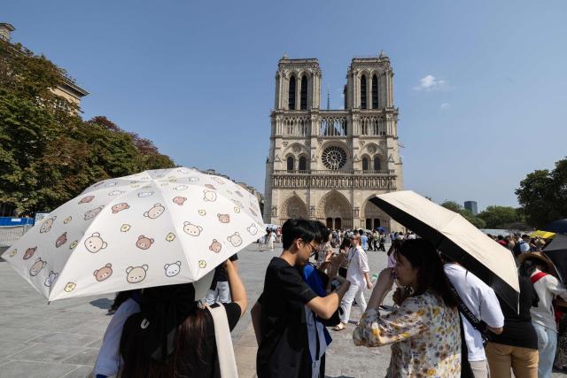 Tourists use umbrellas to shield themselves from the sun as they queue to visit Notre-Dame Cathedral during a hot summer day in Paris on July 25, 2026. (Photo by Xavier GALIANA / AFP)