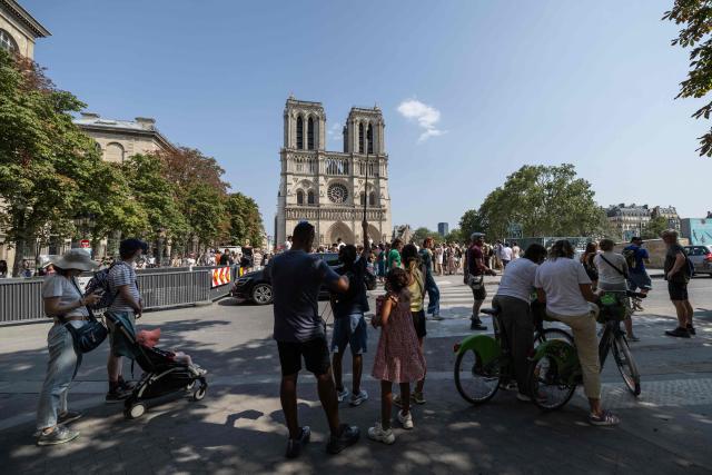 Tourists stand in a shaded area in front of Notre-Dame Cathedral during a hot summer day in Paris on July 25, 2026. (Photo by Xavier GALIANA / AFP)
