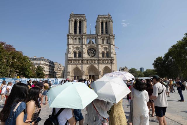 Tourists use umbrellas to shield themselves from the sun as they queue to visit Notre-Dame Cathedral during a hot summer day in Paris on July 25, 2026. (Photo by Xavier GALIANA / AFP)