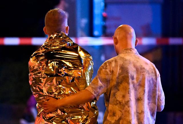 A man comforts another one who is wrapped in a security blanket near the scene where one person was killed and around 15 injured after a car is believed to have hit the crowd on the outskirts of the Christopher Street Day (CSD) parade in Berlin, on July 25, 2026. "We believe that a vehicle entered the Tiergarten park and hit several people and injured them," police posted on social media. The injured were being treated by the emergency services and they were actively seeking the people responsible, they added. (Photo by RALF HIRSCHBERGER / AFP)