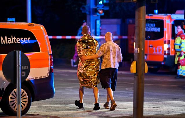 A man comforts another one who is wrapped in a security blanket near the scene where one person was killed and 16 injured after a car is believed to have hit the crowd on the outskirts of the Christopher Street Day (CSD) parade in Berlin, on July 25, 2026. "We believe that a vehicle entered the Tiergarten park and hit several people and injured them," police posted on social media. The injured were being treated by the emergency services and they were actively seeking the people responsible, they added. (Photo by RALF HIRSCHBERGER / AFP)
