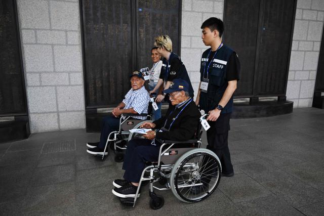 Colombian veterans of the Korean War, Jovino Paez Diaz (R) and Jose Olmedo Rojas Marin are wheeled past a monument with the names of fellow soldiers from United Nations countries, who were killed in the Korean War, during a visit to the Korean War Memorial in Seoul on July 26, 2026. Seventy-four participants from 21 countries, including 13 UN Korean War veterans and bereaved family members are visiting Seoul as part of the Revisit Korea Program for UN Korean War Veterans. (Photo by GREG BAKER / AFP)