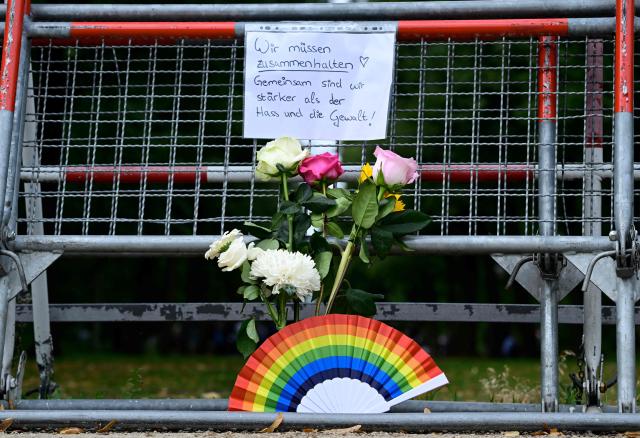 A, inscription reading "We need to stick together! Together we are stronger than hate and violence" has been attached on a barrier next to a bouquet of flowers and a rainbow colloured fan in commemoration for the victims on July 26, 2026 near the site in the Tiergarten park in Berlin, where a car was driven the evening before into people killing one person and injuring 16 on the outskirts of the Christopher Street Day (CSD) parade. German police searched on July 26, 2026 for a suspect believed linked to Islamist circles after a car ploughed into a crowd near Berlin's Gay Pride celebrations, killing one person and wounding 16 others. The incident shattered what had been a day of celebration for hundreds of thousands attending Christopher Street Day, one of Europe's largest Pride events, and left revellers fleeing a central Berlin park as sirens echoed through the night. (Photo by John MACDOUGALL / AFP)