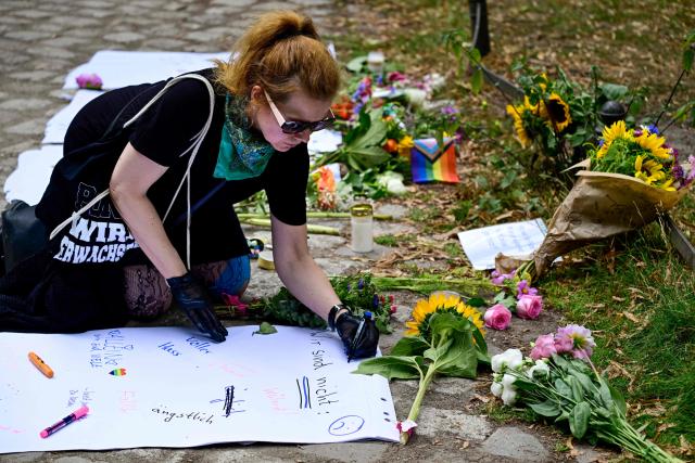 A bwoman writes thoughts on a paper at a makeshift commemoration site for the victims on July 26, 2026 near the site in the Tiergarten park in Berlin, where a car was driven the evening before into people killing one person and injuring 16 on the outskirts of the Christopher Street Day (CSD) parade. German police searched on July 26, 2026 for a suspect believed linked to Islamist circles after a car ploughed into a crowd near Berlin's Gay Pride celebrations, killing one person and wounding 16 others. The incident shattered what had been a day of celebration for hundreds of thousands attending Christopher Street Day, one of Europe's largest Pride events, and left revellers fleeing a central Berlin park as sirens echoed through the night. (Photo by John MACDOUGALL / AFP)