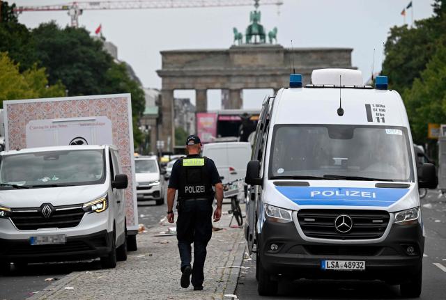 Police patrols while cleaning operations are underway on Strasse des 17. Juni street in front of Brandenburg Gate in Berlin on July 26, 2026 one day after the Christopher Street Day (CSD) parade in Berlin, that had to be stopped after a after a car ploughed into people outside the celebrations. German police searched on July 26, 2026 for a suspect believed linked to Islamist circles after a car ploughed into a crowd near Berlin's Gay Pride celebrations, killing one person and wounding 16 others. The incident shattered what had been a day of celebration for hundreds of thousands attending Christopher Street Day, one of Europe's largest Pride events, and left revellers fleeing a central Berlin park as sirens echoed through the night. (Photo by RALF HIRSCHBERGER / AFP)