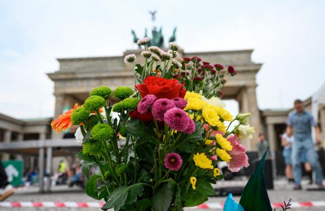 A bouquet of flowers is displayed on July 26, 2026 in front of landmark Brandenburg Gate prior to a so-called "community mourning" one day after the car ramming attack on people on the outskirts of Berlin's Christopher Street Day (CSD) parade on late July 25, 2026, killing one person and injuring 16 in the Tiergarten park. German police searched on July 26, 2026 for a suspect believed linked to Islamist circles after a car ploughed into a crowd near Berlin's Gay Pride celebrations, killing one person and wounding 16 others. The incident shattered what had been a day of celebration for hundreds of thousands attending Christopher Street Day, one of Europe's largest Pride events, and left revellers fleeing a central Berlin park as sirens echoed through the night. (Photo by RALF HIRSCHBERGER / AFP)