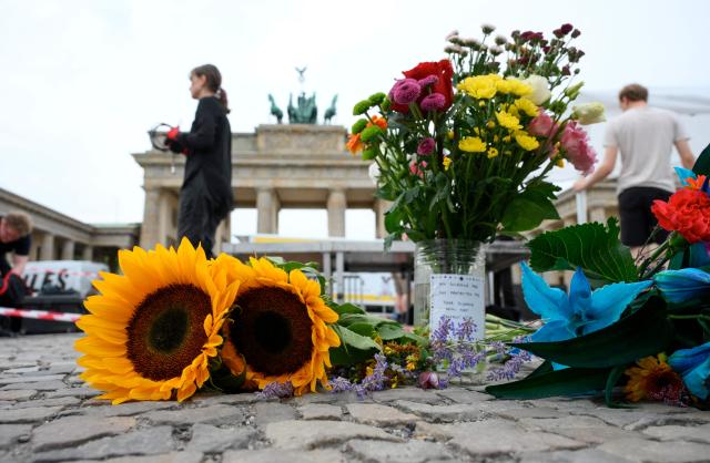 People set up bouquets of flowers on July 26, 2026 in front of landmark Brandenburg Gate prior to a so-called "community mourning" one day after the car ramming attack on people on the outskirts of Berlin's Christopher Street Day (CSD) parade on late July 25, 2026, killing one person and injuring 16 in the Tiergarten park. German police searched on July 26, 2026 for a suspect believed linked to Islamist circles after a car ploughed into a crowd near Berlin's Gay Pride celebrations, killing one person and wounding 16 others. The incident shattered what had been a day of celebration for hundreds of thousands attending Christopher Street Day, one of Europe's largest Pride events, and left revellers fleeing a central Berlin park as sirens echoed through the night. (Photo by RALF HIRSCHBERGER / AFP)