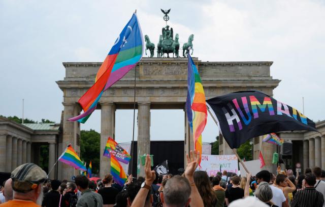 Demonstrators wave rainbow peace flags on July 26, 2026 in front of landmark Brandenburg Gate during to a so-called "community mourning" one day after the car ramming attack on people on the outskirts of Berlin's Christopher Street Day (CSD) parade on late July 25, 2026, killing one person and injuring 16 in the Tiergarten park. German police searched on July 26, 2026 for a suspect believed linked to Islamist circles after a car ploughed into a crowd near Berlin's Gay Pride celebrations, killing one person and wounding 16 others. The incident shattered what had been a day of celebration for hundreds of thousands attending Christopher Street Day, one of Europe's largest Pride events, and left revellers fleeing a central Berlin park as sirens echoed through the night. (Photo by RALF HIRSCHBERGER / AFP)