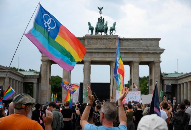 Demonstrators wave rainbow peace flags on July 26, 2026 in front of landmark Brandenburg Gate during to a so-called "community mourning" one day after the car ramming attack on people on the outskirts of Berlin's Christopher Street Day (CSD) parade on late July 25, 2026, killing one person and injuring 16 in the Tiergarten park. German police searched on July 26, 2026 for a suspect believed linked to Islamist circles after a car ploughed into a crowd near Berlin's Gay Pride celebrations, killing one person and wounding 16 others. The incident shattered what had been a day of celebration for hundreds of thousands attending Christopher Street Day, one of Europe's largest Pride events, and left revellers fleeing a central Berlin park as sirens echoed through the night. (Photo by RALF HIRSCHBERGER / AFP)