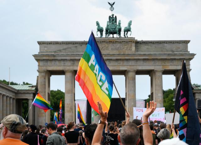 Demonstrators wave rainbow peace flags on July 26, 2026 in front of landmark Brandenburg Gate during to a so-called "community mourning" one day after the car ramming attack on people on the outskirts of Berlin's Christopher Street Day (CSD) parade on late July 25, 2026, killing one person and injuring 16 in the Tiergarten park. German police searched on July 26, 2026 for a suspect believed linked to Islamist circles after a car ploughed into a crowd near Berlin's Gay Pride celebrations, killing one person and wounding 16 others. The incident shattered what had been a day of celebration for hundreds of thousands attending Christopher Street Day, one of Europe's largest Pride events, and left revellers fleeing a central Berlin park as sirens echoed through the night. (Photo by RALF HIRSCHBERGER / AFP)