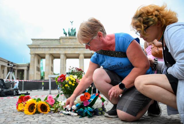 Mourners place bouquets of flowers on July 26, 2026 in front of landmark Brandenburg Gate during to a so-called "community mourning" one day after the car ramming attack on people on the outskirts of Berlin's Christopher Street Day (CSD) parade on late July 25, 2026, killing one person and injuring 16 in the Tiergarten park. German police searched on July 26, 2026 for a suspect believed linked to Islamist circles after a car ploughed into a crowd near Berlin's Gay Pride celebrations, killing one person and wounding 16 others. The incident shattered what had been a day of celebration for hundreds of thousands attending Christopher Street Day, one of Europe's largest Pride events, and left revellers fleeing a central Berlin park as sirens echoed through the night. (Photo by RALF HIRSCHBERGER / AFP)
