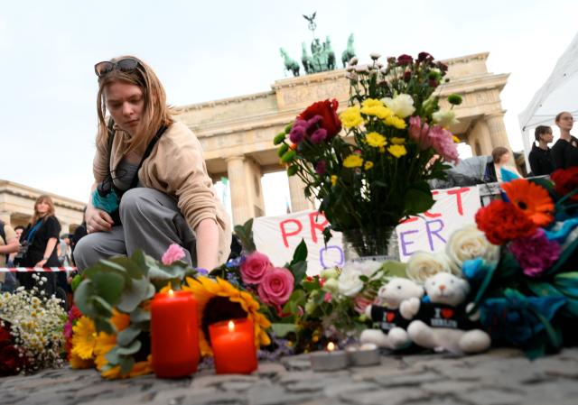 A mourner places flowers on July 26, 2026 in front of landmark Brandenburg Gate during to a so-called "community mourning" one day after the car ramming attack on people on the outskirts of Berlin's Christopher Street Day (CSD) parade on late July 25, 2026, killing one person and injuring 16 in the Tiergarten park. German police searched on July 26, 2026 for a suspect believed linked to Islamist circles after a car ploughed into a crowd near Berlin's Gay Pride celebrations, killing one person and wounding 16 others. The incident shattered what had been a day of celebration for hundreds of thousands attending Christopher Street Day, one of Europe's largest Pride events, and left revellers fleeing a central Berlin park as sirens echoed through the night. (Photo by RALF HIRSCHBERGER / AFP)