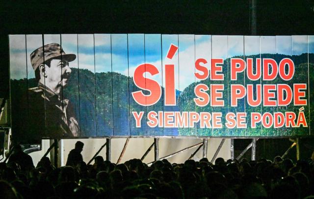 Cubans stand next to a billboard depicting former President (2006-2018) Raul Castro and reading "Yes, it was possible, it is possible, and it always will be possible" during the 73rd anniversary celebration of the guerrilla assault on the Moncada Barracks, led by the late leader Fidel Castro and considered the start of the Cuban Revolution, in Pinar del Rio, Cuba, on July 26, 2026. (Photo by YAMIL LAGE / AFP)