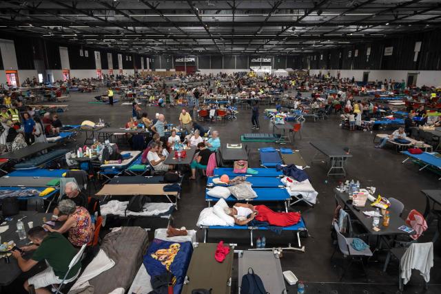 People gather at an exhibition centre being used for people displaced by the wildfires, in Bordeaux, southwestern France on July 26, 2026. France fought an "unpredictable" wildfire close to Bordeaux on July 26, 2026 while Spain warned of "difficult hours" in its own fiery battle, with evacuations from danger zones in both countries mounting to well over 300,000 people. Scientists have long warned that climate change caused by human use of fossil fuels will make periods of drought more intense and longer-lasting, creating the ideal conditions for wildfires. (Photo by Ed JONES / AFP)
