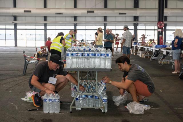 Staff members prepare bottles of water at an exhibition centre being used for people displaced by the wildfires, in Bordeaux, southwestern France on July 26, 2026. France fought an "unpredictable" wildfire close to Bordeaux on July 26, 2026 while Spain warned of "difficult hours" in its own fiery battle, with evacuations from danger zones in both countries mounting to well over 300,000 people. Scientists have long warned that climate change caused by human use of fossil fuels will make periods of drought more intense and longer-lasting, creating the ideal conditions for wildfires. (Photo by Ed JONES / AFP)