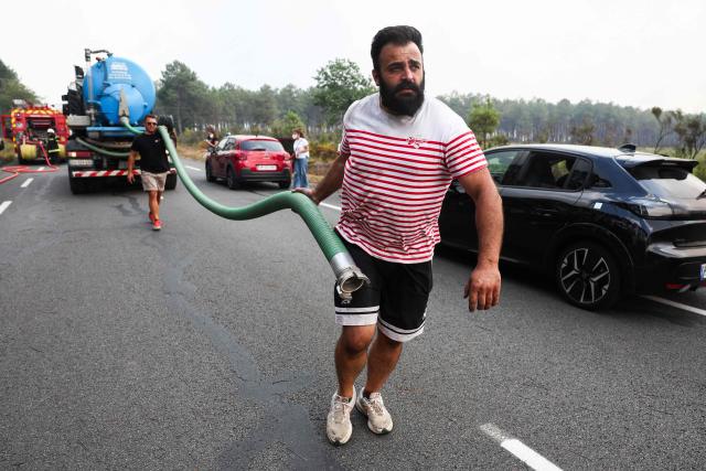 Volunteers hold a hose during a wildfire in a forest near Marcheprime, some 30km from Bordeaux, on July 26, 2026 as a wildfire has been ravaging the forest north of the Arcachon Basin (Gironde). The 220,000 people evacuated due to the massive wildfire in France's Gironde region will not be able to return home "until the fire has been brought under control", the local prefect said, also ruling out any normal workday on Monday in the affected towns, ahead of a possible worsening of the situation on Tuesday due to an expected rise in temperatures. (Photo by ROMAIN PERROCHEAU / AFP)
