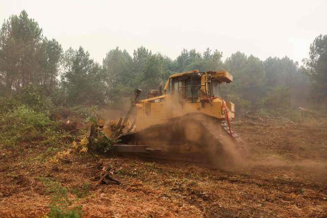An excavator tears out trees to construct a firebreak in a forest near Cestas, some 17km from Bordeaux, on July 26, 2026 as a wildfire has been ravaging the forest north of the Arcachon Basin (Gironde). The 220,000 people evacuated due to the massive wildfire in France's Gironde region will not be able to return home "until the fire has been brought under control", the local prefect said, also ruling out any normal workday on Monday in the affected towns, ahead of a possible worsening of the situation on Tuesday due to an expected rise in temperatures. (Photo by ROMAIN PERROCHEAU / AFP)