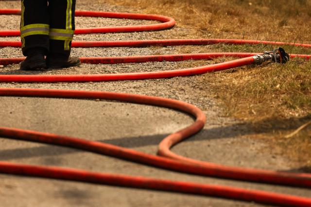 A firefighter stands next to a fire hose during a wildfire in a forest near Marcheprime, some 30km from Bordeaux, on July 26, 2026 as a wildfire has been ravaging the forest north of the Arcachon Basin (Gironde). The 220,000 people evacuated due to the massive wildfire in France's Gironde region will not be able to return home "until the fire has been brought under control", the local prefect said, also ruling out any normal workday on Monday in the affected towns, ahead of a possible worsening of the situation on Tuesday due to an expected rise in temperatures. (Photo by ROMAIN PERROCHEAU / AFP)