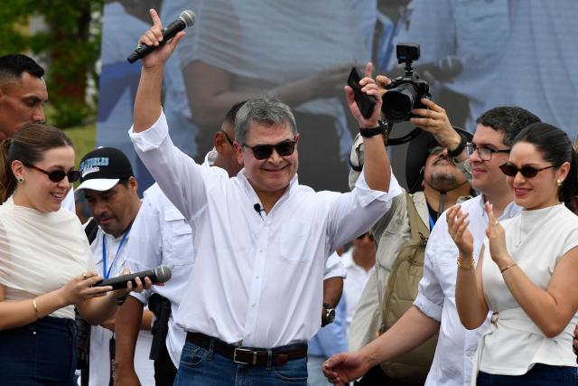 Former Honduras' President (2014-2022) Juan Orlando Hernandez waves flanked by his daughters Daniela (L) and Isabela (R) during a welcome event at an estate, in Comayagua, 80 km north of Tegucigalpa, on July 26, 2026. Hernandez returned to Honduras on a private flight to face corruption charges after being pardoned last year by US President Donald Trump following a 45-year drug trafficking sentence, ahead of a presidential election won by fellow conservative Nasry Asfura. (Photo by Orlando SIERRA / AFP)