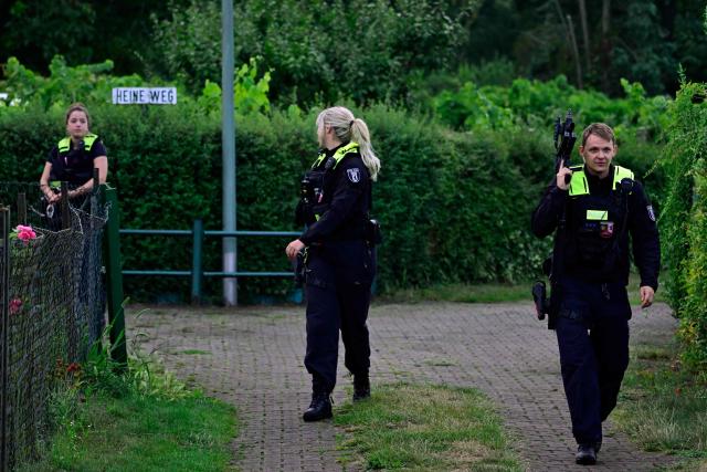 Police officers with automatic weapons walk in an allotment complex in the western Spandau district of Berlin on July 26, 2026, in a garden area near the scene where the chief suspect in the previous nights' deadly attack near Berlin's Pride parade has been shot dead. German police searched on July 26, 2026 for a suspect believed linked to Islamist circles after a car ploughed into a crowd near Berlin's Gay Pride celebrations, killing one person and wounding 16 others. The incident shattered what had been a day of celebration for hundreds of thousands attending Christopher Street Day, one of Europe's largest Pride events, and left revellers fleeing a central Berlin park as sirens echoed through the night. (Photo by John MACDOUGALL / AFP)