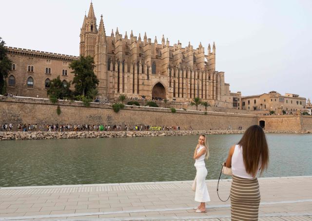 Tourists take pictures near the Cathedral during a demonstration to protest against overtourism and housing prices in Palma de Mallorca, on the Balearic island of Mallorca, on July 26, 2026. (Photo by JAIME REINA / AFP)
