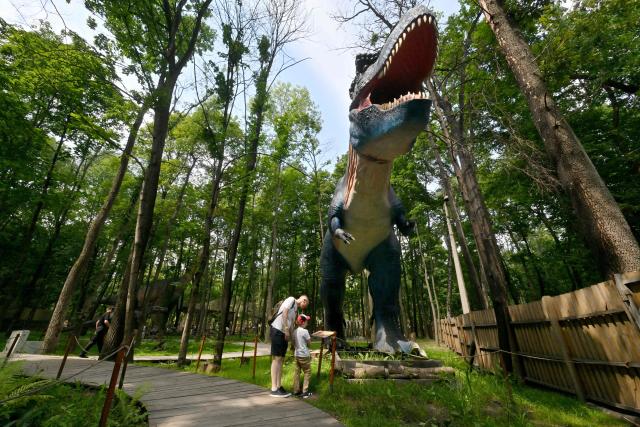 Father and his daughter examine acting dinosaur replica in the park of the National Exhibition Centre in Kyiv during warm sunny day on July 26, 2026, amid Russian invasion in Ukraine. (Photo by Sergei SUPINSKY / AFP)